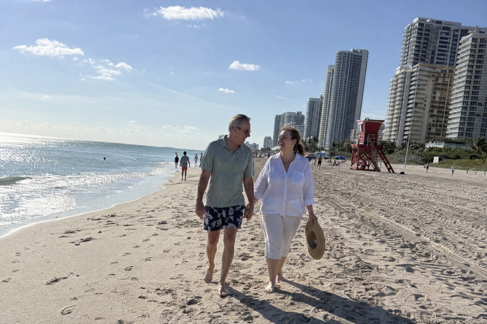 A couple in their sixties walking hand in hand along Sunny Isles Beach