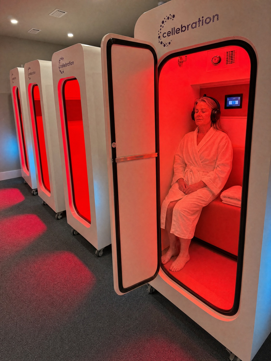 A woman relaxing with headphones on inside a red-lit Cellebration hyperbaric chamber