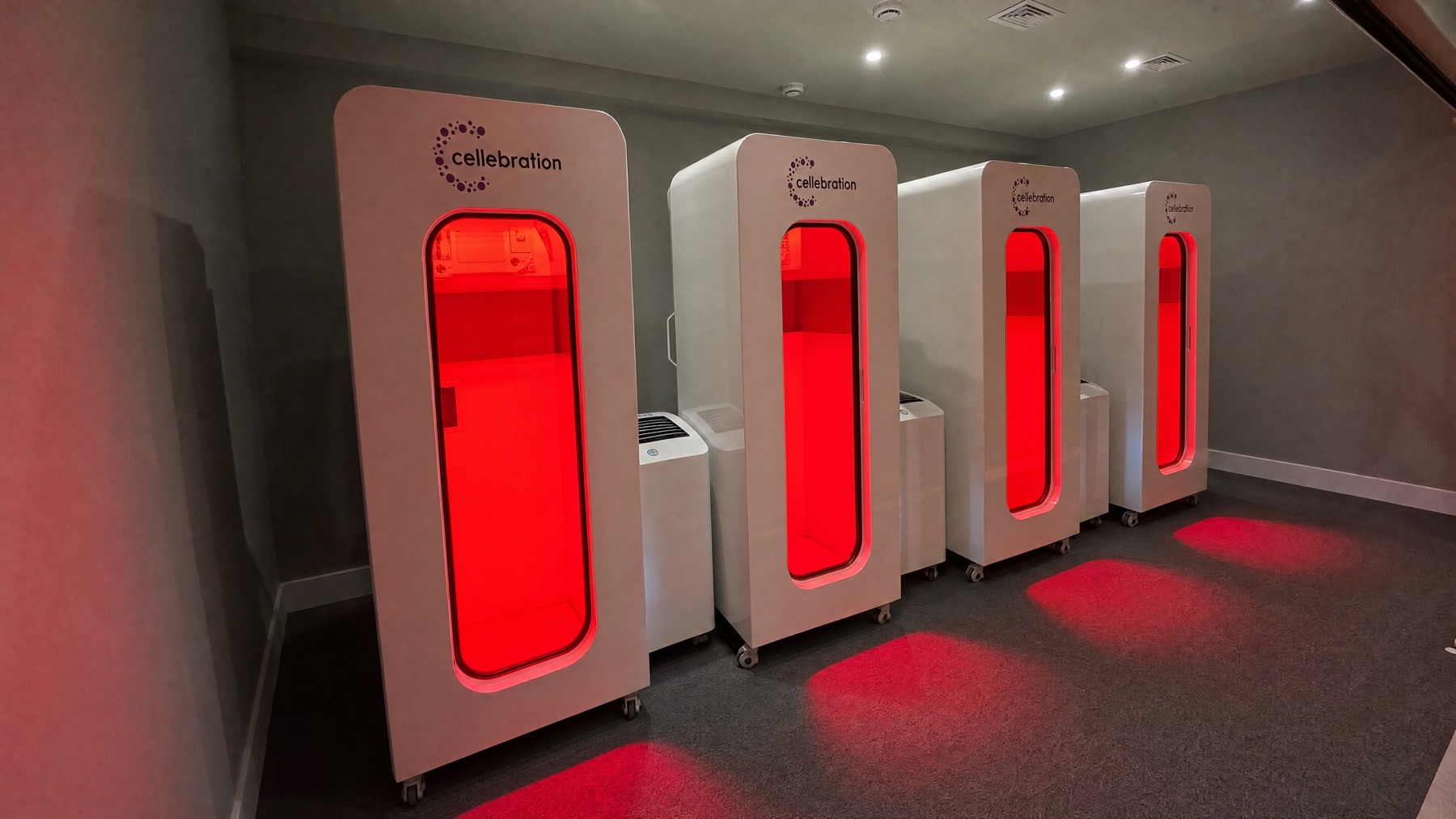 A row of four Cellebration hyperbaric chambers glowing red in the Sunny Isles treatment room